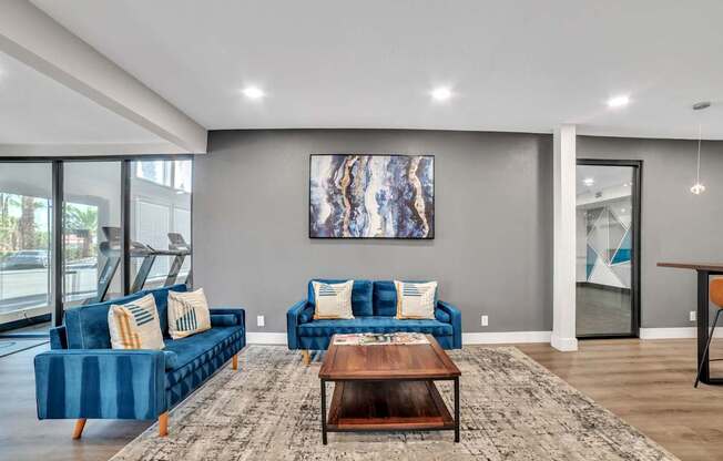 A living room with blue couches and a large painting on the wall.