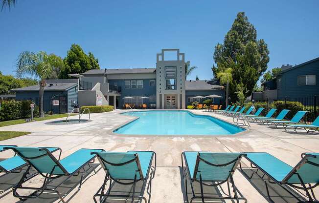 A pool surrounded by lawn chairs in front of a building at Autumn Oaks Apartments, Roseville, CA, 95678