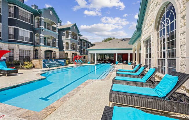 A large swimming pool with lounge chairs and a building in the background.