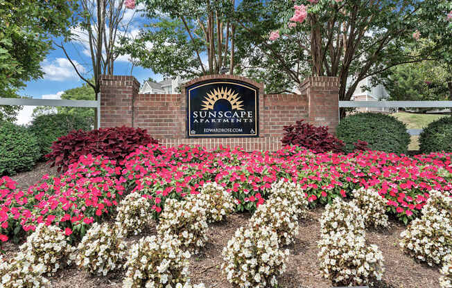 A sign for SunScape Apartments is surrounded by flowers.