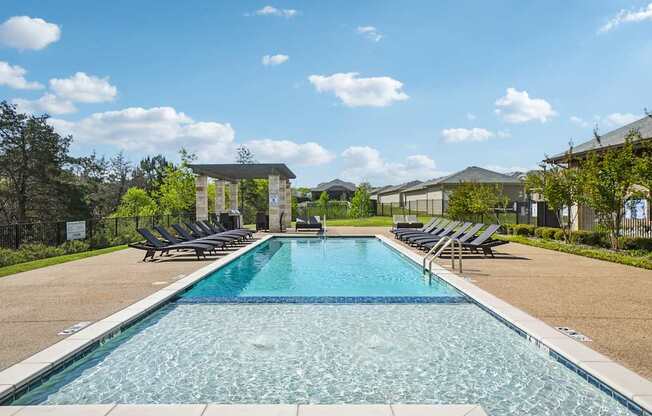 A large swimming pool with lounge chairs and a building in the background.