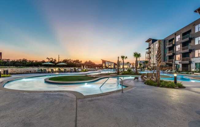 A large outdoor swimming pool surrounded by a concrete patio and a building in the background.