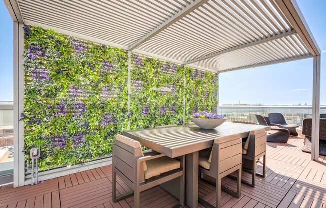 A table and chairs are set up on a patio with a green wall behind it.