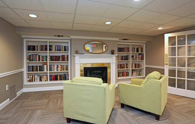 a library with two green chairs and a fireplace