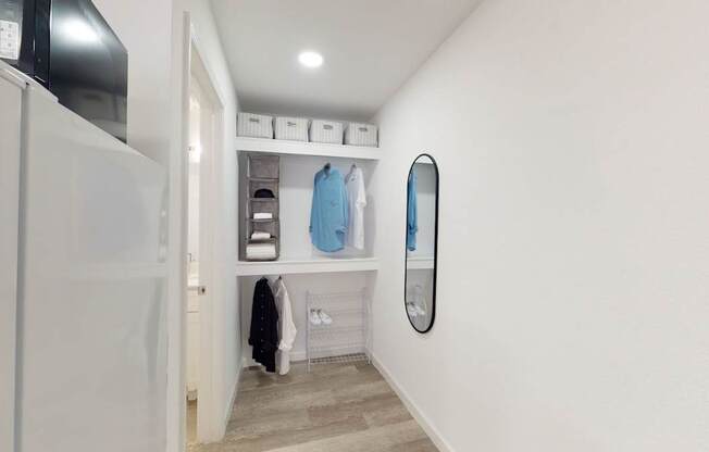 A white wall with a mirror and a shelf with clothes hanging on it.