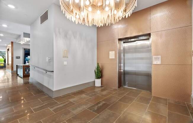 A large, modern chandelier hangs over a reception desk in a well-lit hallway.