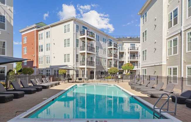 A swimming pool surrounded by lounge chairs and buildings in the background.