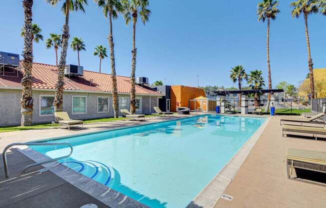 A pool surrounded by palm trees and a building in the background.