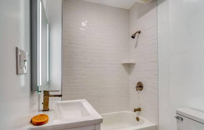 A white bathroom with a sink, mirror, and bathtub.