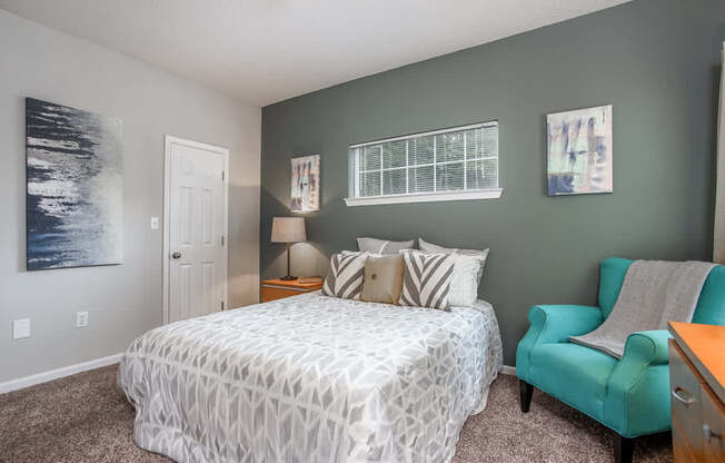 A bedroom with a bed, chair, and two pictures on the wall.