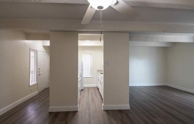 A view from the dining room with white ceiling fan looking towards the kitchen and entryway with hardwoodlike flooring throughout in a 2 bedroom, 2 bath with balcony apartment home at Harvard Square Apartments in the Vickery Midtown neighborhood of Dallas, TX.