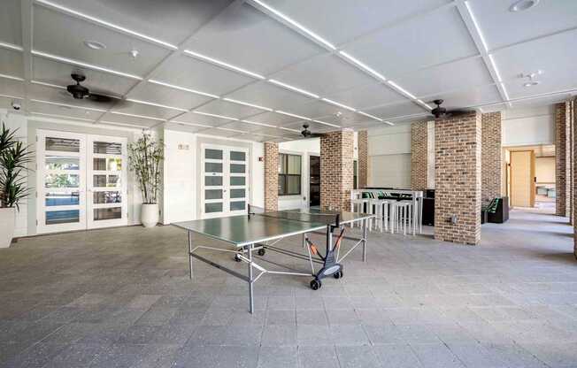 A ping pong table is in the middle of a room with a brick column.