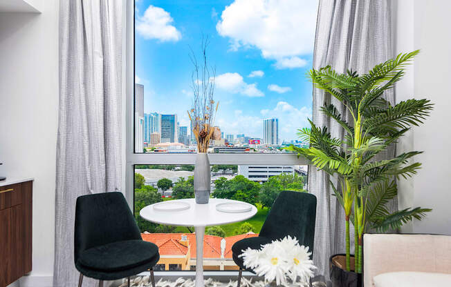 a small white table with two black chairs sits in front of a large window with a view