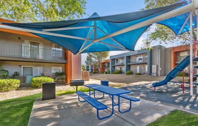 Outdoor BBQ Area with Blue Canopy and Picnic Table at Indigo Park Apartments in Albuquerque, NM.