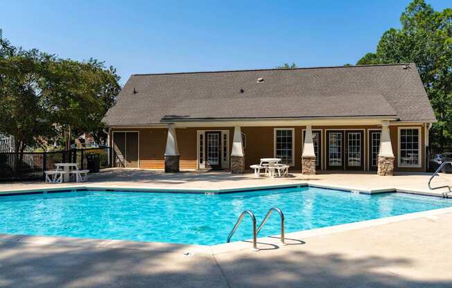 A pool in front of a house with a patio.