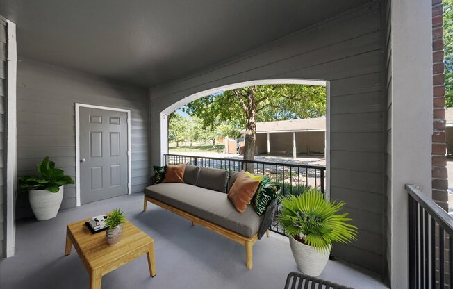A balcony with a sofa, table, and potted plants. at Somerset Oaks Apartment Homes, Olathe, KS, 66062