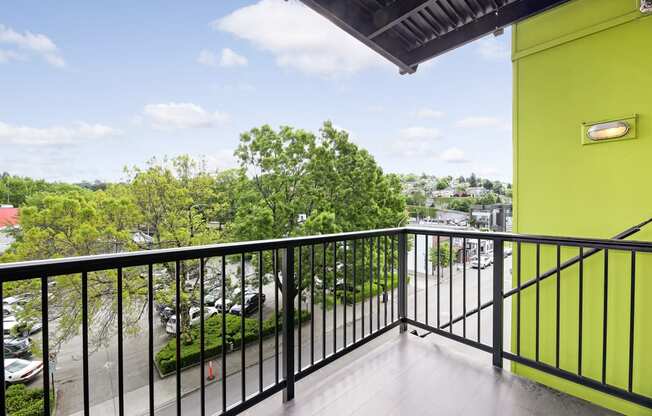 A balcony with a black railing and a view of a parking lot and trees.