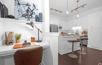 A modern home office with a desk, chair, and a kitchen in the background.