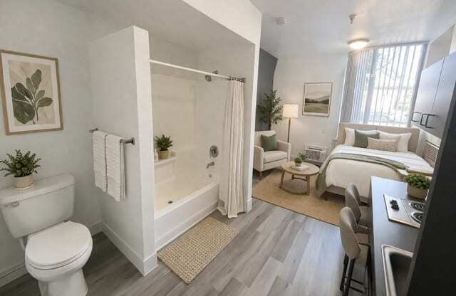 A modern bathroom with a white toilet, a bathtub with a shower curtain, a bed, and a desk with a computer.