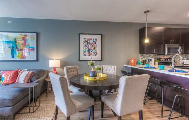 a dining area with a table and chairs and a kitchen in the background