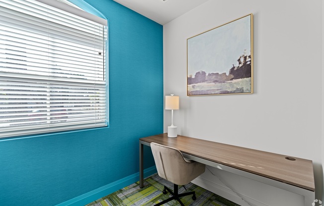 A room with a desk, chair, and a painting on the wall.