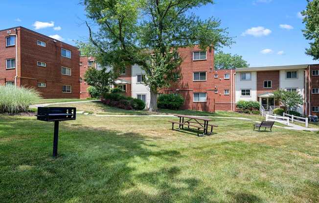 A grassy area with a picnic table and bench in front of apartment buildings.