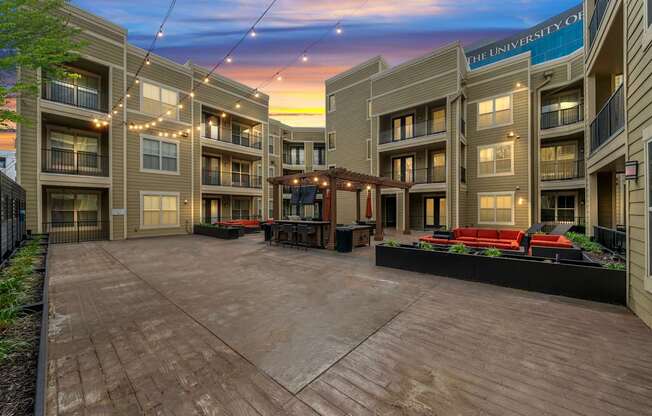 Outdoor common area at West 39th Street Apartments with lounge furniture, string lights, and backdrop of The University of Kansas City.