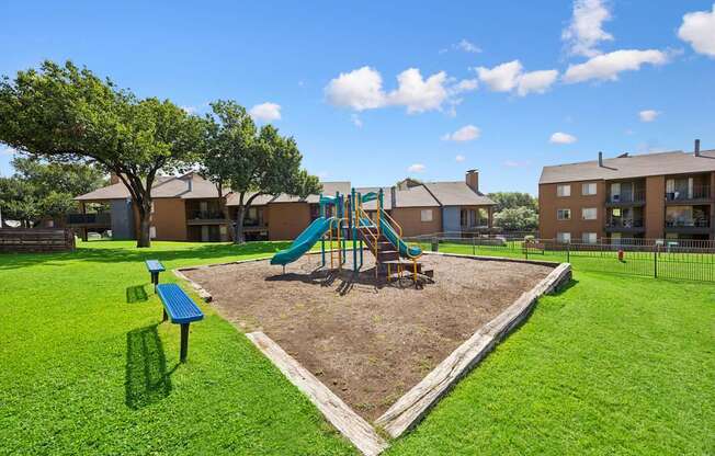A playground with a green slide and a brown tree.