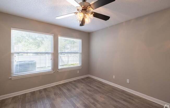A room with a ceiling fan and two windows.