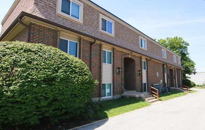 A red brick house with a green bush in front.