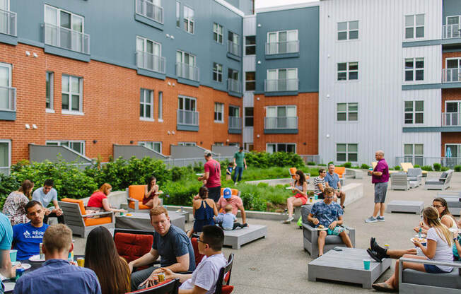 a group of people sitting and standing on a patio in front of an apartment building