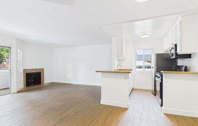A spacious kitchen and living room with wood flooring and white walls.