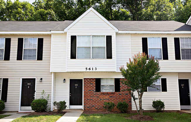 A white house with black shutters and a brick wall in front.