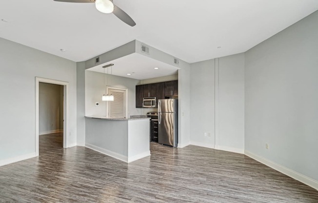 an empty living room with a kitchen and a ceiling fan