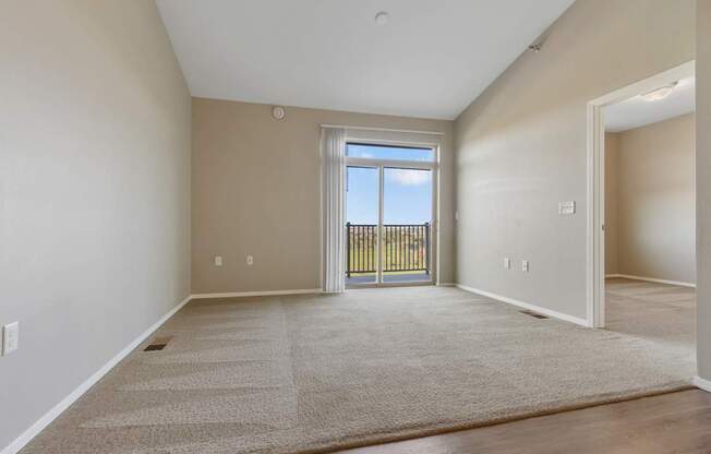 A spacious room with a carpeted floor and a view of a fence through a glass door.