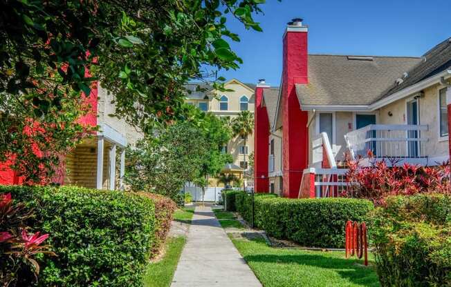 Fusion Orlando apartments pathway lined with lush landscaping and two story apartment buildings with red chimneys and outdoor stairs.