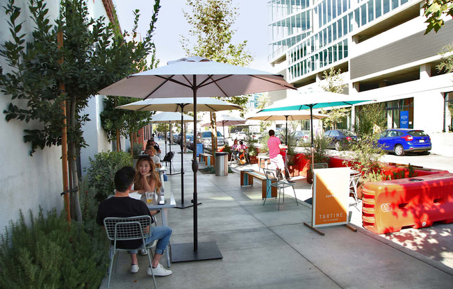 A man and woman are sitting at a table under an umbrella in a courtyard.
