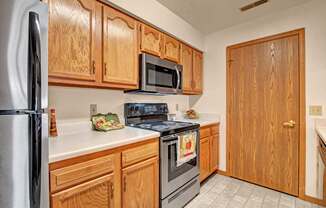 A bright kitchen here at Arbor Ridge featuring warm wood cabinets, white countertops, and stainless steel appliances. The functional layout and clean finishes create a welcoming, practical space for everyday cooking.