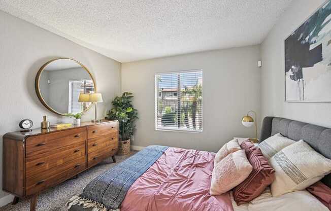 A bedroom with a bed, dresser, mirror, and window.