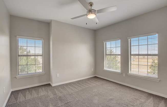 A room with a ceiling fan and two windows.
