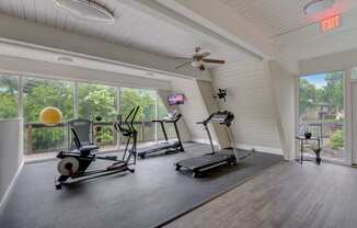 two treadmills and other exercise equipment in a room with large windows