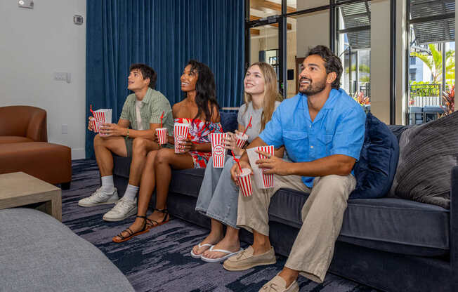 Four people sitting on a couch eating popcorn.