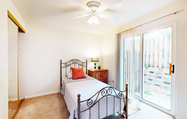 A bedroom with a bed, a ceiling fan, and a sliding glass door.