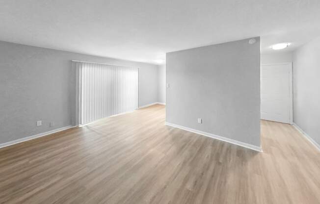 the living room and dining room of an apartment with wood flooring and white walls