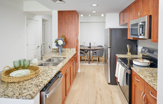 Newly Renovated Ellington Floor Plan Kitchen at Meridian at Grosvenor Station featuring sleek stainless steel appliances, modern vinyl plank wood-style flooring, and updated lighting fixtures that complement existing granite countertops and custom cabinetry.