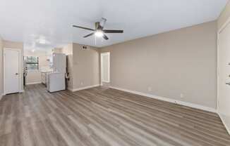 a living room with a ceiling fan and a kitchen in the background