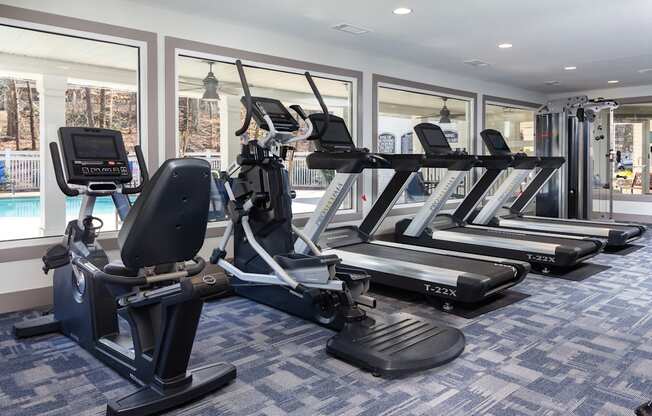 a gym with treadmills and other exercise equipment in a room with windows