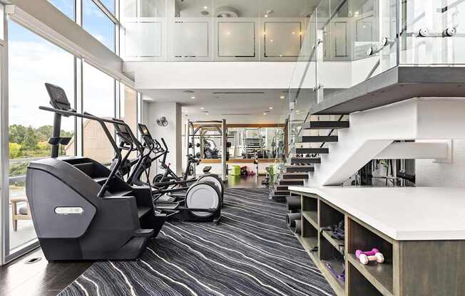 A gym with a treadmill, elliptical machines and a staircase.