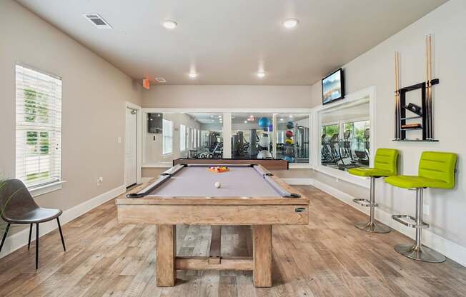 A pool table is in the middle of a room with a chair and a TV mounted on the wall.