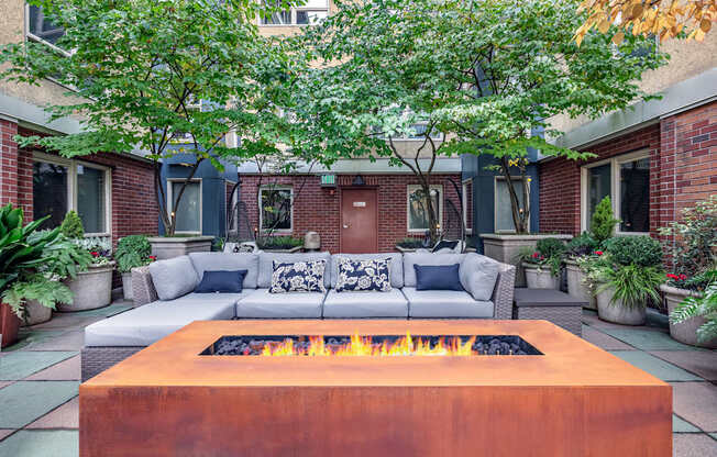 A fire pit in the middle of a patio surrounded by a white couch and potted plants.